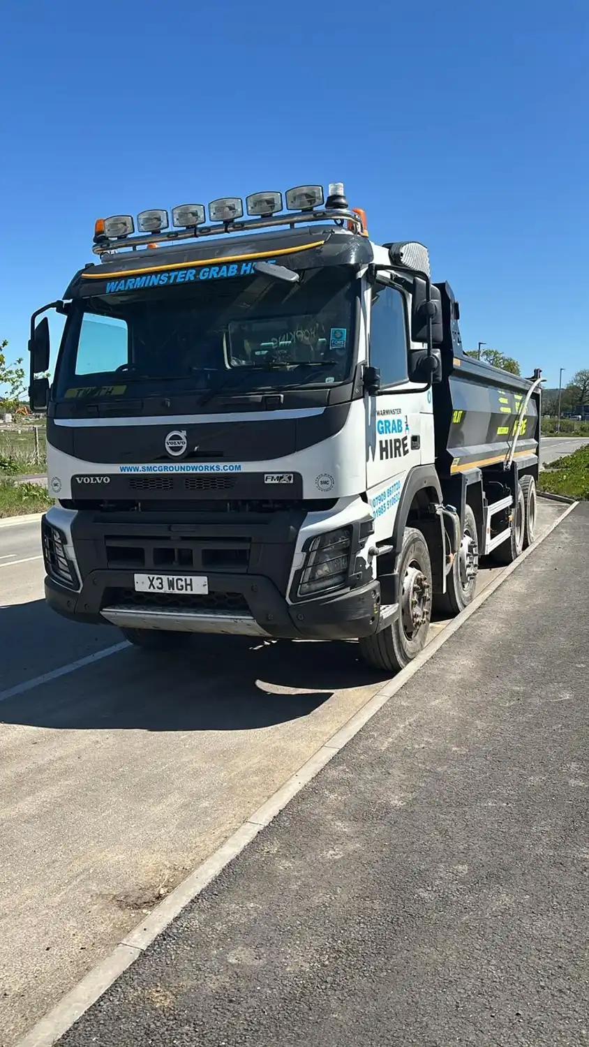 White and black Volvo FMX grab hire lorry parked on the roadside under clear blue sky.